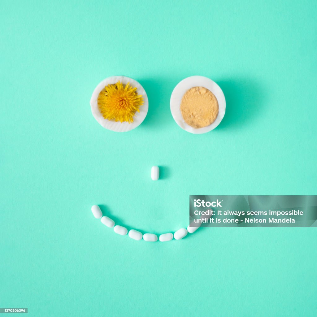 Smiling face made of boiled eggs, yellow flower and candy on light pastel green background. Creative concept, flat lay. Abstract Stock Photo