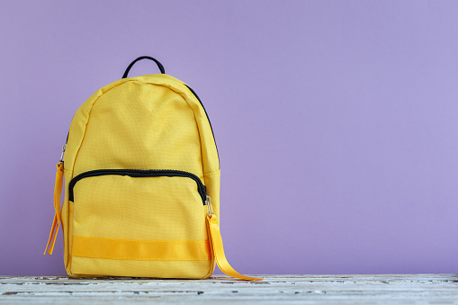 One yellow backpack on a empty purple background with copyspace. Back to school concept.