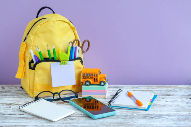 istock Full yellow school backpack with stationery on table on purple background. 1370313179