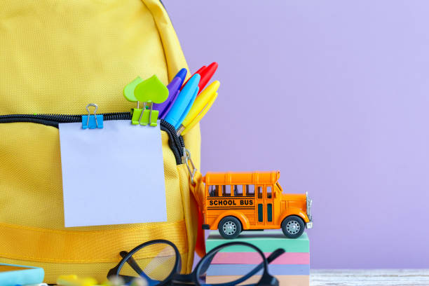 istock Full yellow school backpack with stationery on table on purple background. 1370313187