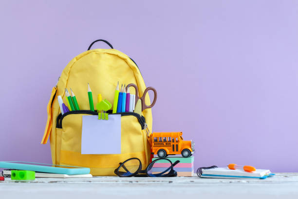 Full yellow school backpack with stationery on table on purple background.