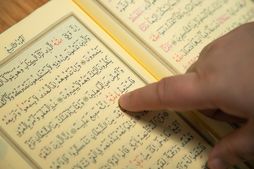 leyendo el Corán y señalando la palabra de Allah con el dedo. letra árabe de versículos del Corán photo