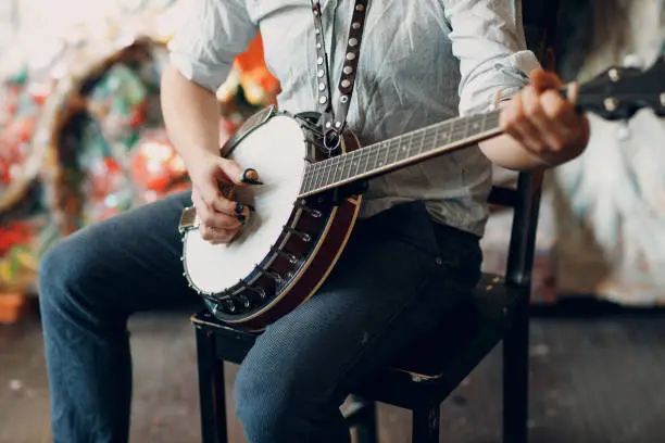 Male musician playing banjo sitting chair indoor closeup