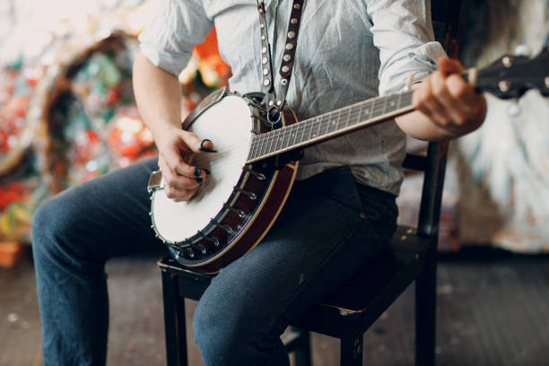 male musician playing banjo sitting chair indoor - folk music imagens e fotografias de stock