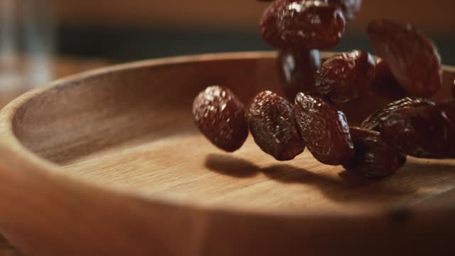 In a beautiful light, dried date fruit fall into the wooden plate.