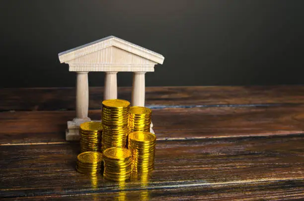 Photo of Bank building and coins stacks. State debt. Budget. Tax collection. Investments in education, museums and libraries, government institutions. Bank capitalization. Financial system, commerce and trade.