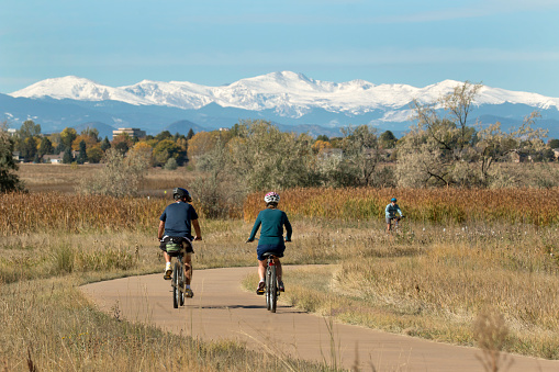 Riding the paved path around the lake with a snowy Mount Evans in the background, visitors enjoy riding their bicycles in Colorado's Cheery Creek State Park.