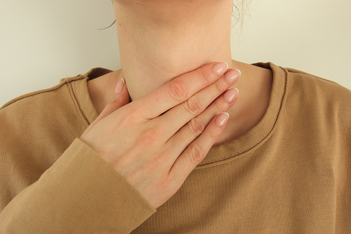 Young woman having sore throat is touching her ill neck. Healthcare and medical concept