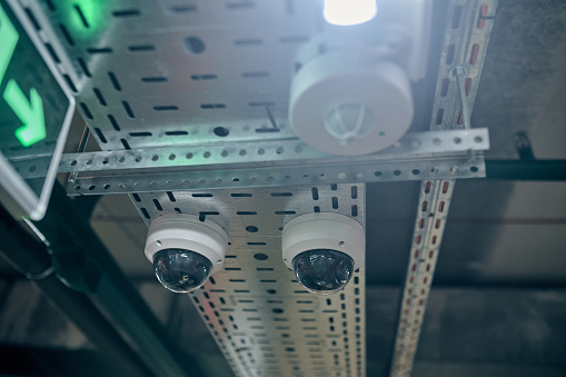 Warehouse security equipment and the fire alarm system mounted on the ceiling beside the exit sign with a green arrow