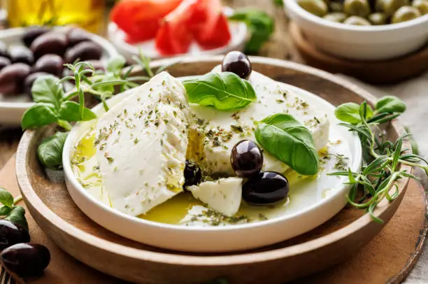 Feta cheese with the addition of olive oil, olives and herbs on a ceramic plate on a rustic wooden table. Traditional Greek products