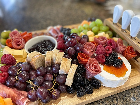 Surface level tabletop view charcuterie board fresh fruit cured meats cheeses nuts crackers bread, French-inspired branch of cooking, delicious healthy appetizers on bamboo plater or board, social event dinner party soirée.
