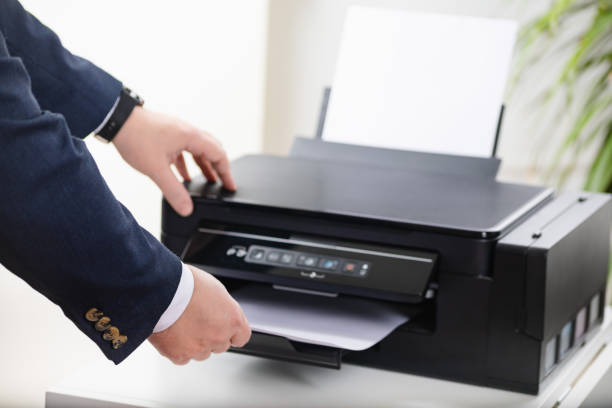 istock Businessman operating printer in office. Close up of hands taking paper from printer scanner or laser copy machine in office. 1370339319