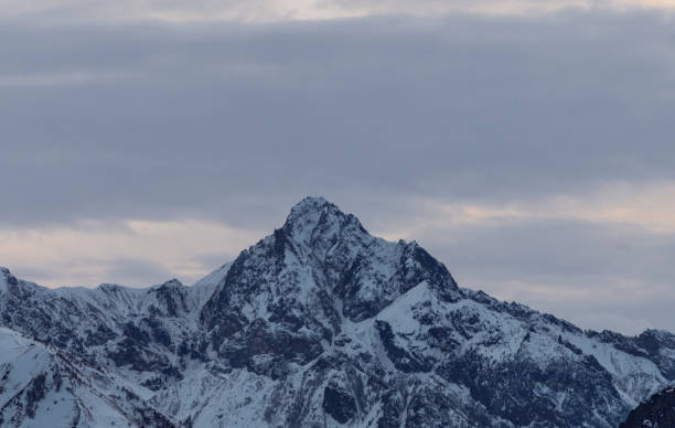 hermoso paisaje de montaña invernal al amanecer con nubes dramáticas. altas montañas cubiertas de nieve en la niebla. - mountain mountain peak environment caucasus fotografías e imágenes de stock