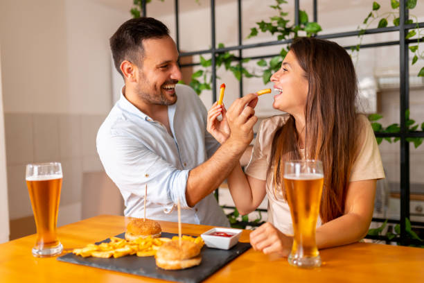Couple having fun eating burgers and drinking beer stock photo