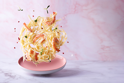 Levitating pasta with shrimps and spices, fettuccine and prawns on a pink background.
