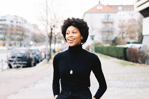 Portrait of a happy young african woman walking down the city street. Female with short curly hair and casuals looking away and smiling.