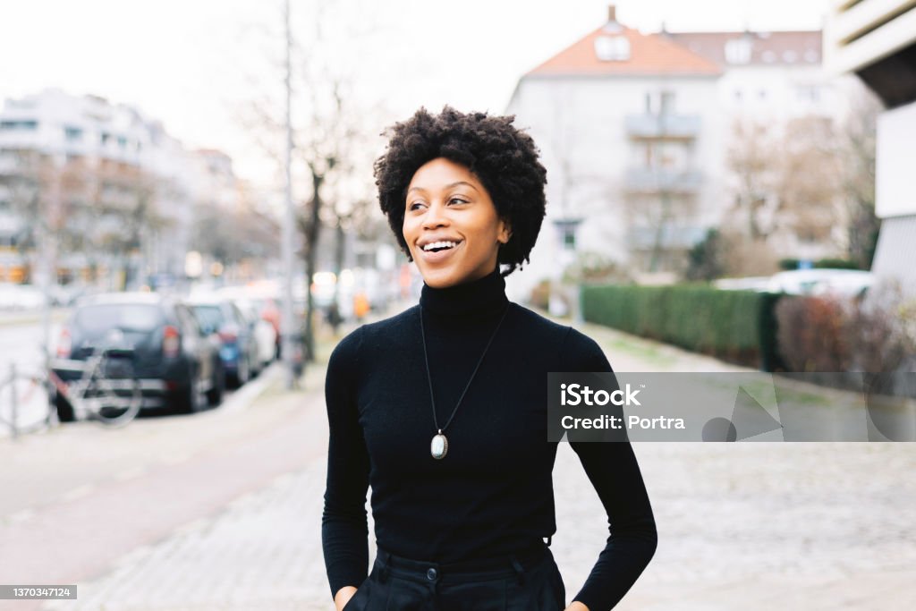Portrait of a happy young African American woman walking down the city street Portrait of a happy young african woman walking down the city street. Female with short curly hair and casuals looking away and smiling. Women Stock Photo