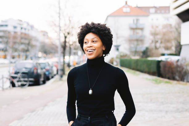 Portrait of a happy young African American woman walking down the city street Portrait of a happy young african woman walking down the city street. Female with short curly hair and casuals looking away and smiling. high collar stock pictures, royalty-free photos & images