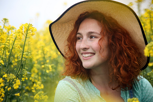 Happy smiling young woman posing in an oilseed or canola field. About 25 years, female Caucasian redhead.
