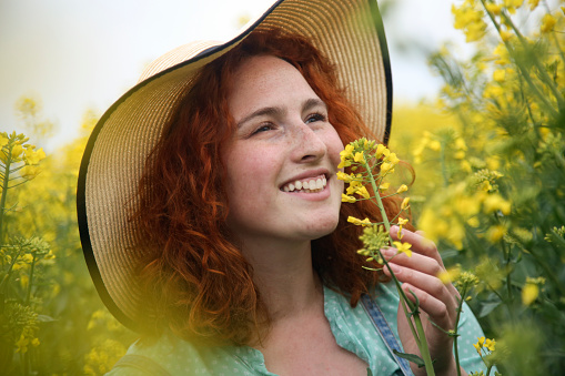 Happy smiling young woman posing in an oilseed or canola field. About 25 years, female Caucasian redhead.