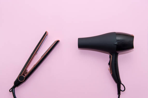 Top view of black hair straightening iron and a hairdryer on pink background. Hair care concept Top view of black hair straightening iron and a hairdryer on pink background. Hair care concept curling tongs photos stock pictures, royalty-free photos & images