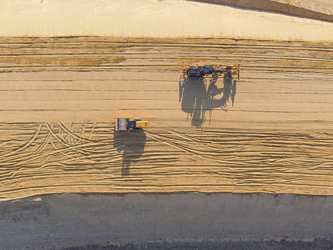 Construction roller and grader on sand, aerial view - photo of construction equipment on a sand road. Construction roller on the sand. A grader on the sand. Bulldozer on the sand. A sandy road. Shadow of construction equipment on the sand. Photo from a drone.