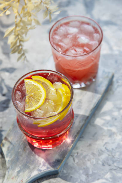istock Two drinks with raspberries and lemon slices in glass glasses on a white board with shadows from tree branches. 1370352168