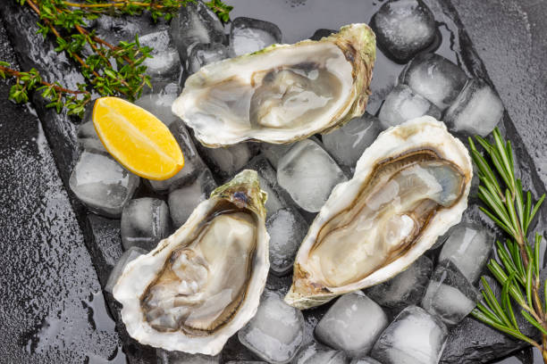 istock Opened oyster shells with ice on black . Lemon and greens on table. 1370353449