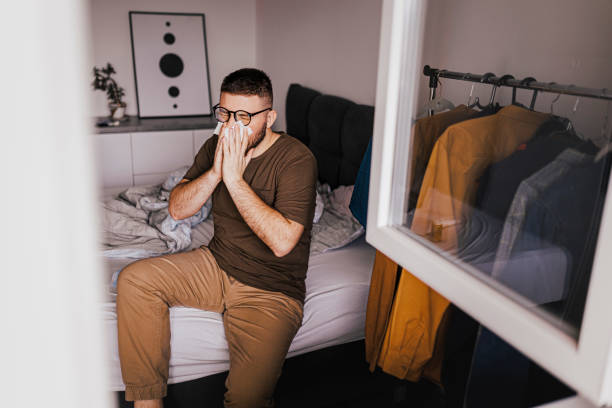 istock Shot of a young man suffering with flu while sitting on bed 1370355943
