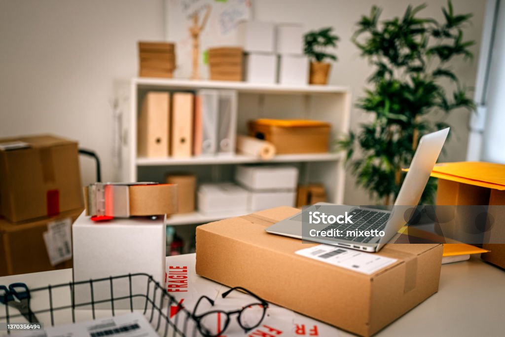 Close-up of laptop with cardboard box on desk in office Close-up of laptop with cardboard boxes by tape dispenser and eyeglasses on desk in retail office Computer Stock Photo