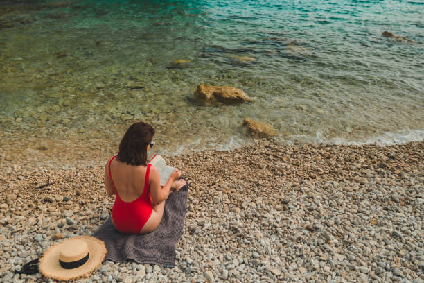 istock woman reading book at sea beach 1370357285