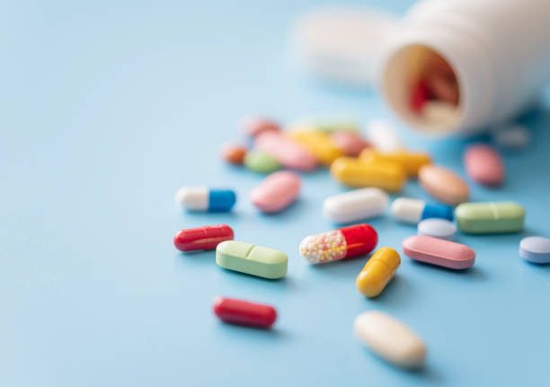 Multicolored Pills scattered from white plastic medicine container Colorful Pills scattered from white plastic pill bottle on blue background. Shallow DOF tablet stock pictures, royalty-free photos & images