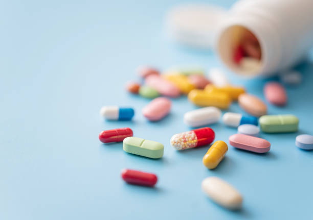 Multicolored Pills scattered from white plastic medicine container Colorful Pills scattered from white plastic pill bottle on blue background. Shallow DOF curing stock pictures, royalty-free photos & images