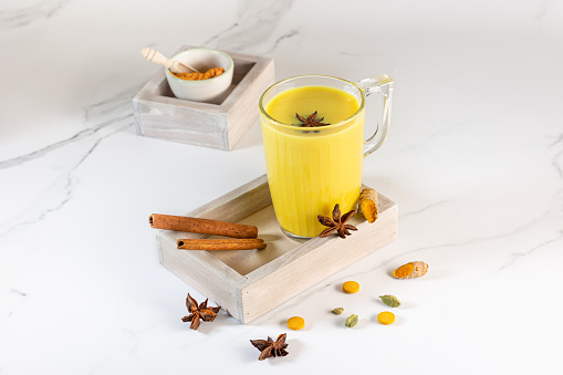 A handmade cup of golden milk with turmeric powder and fresh turmeric root and anise and cinnamon . The concept of spices and herbs. Ayurvedic drink on a light background. Space for text.