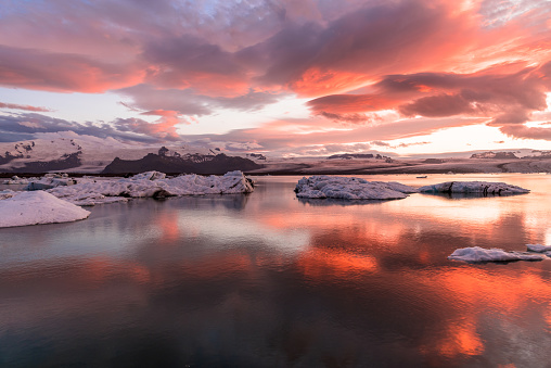 View of a glacier lagoon under a dramatic sky at glowing red in midnight sun in summer Jokulsárlón, Iceland.