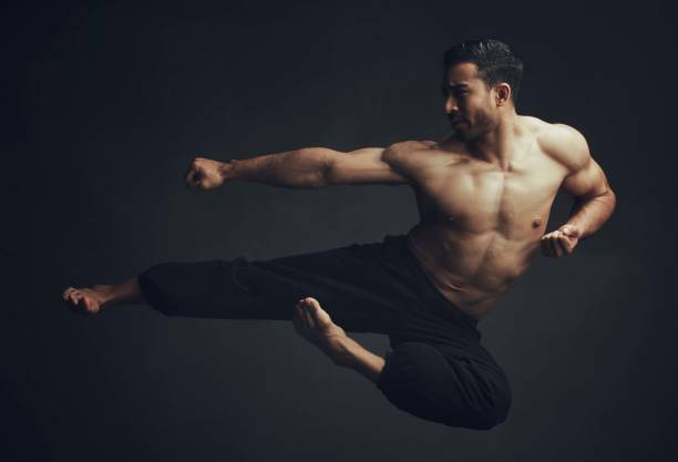 aufnahme in voller länge eines nicht wiederzuerkennenden mannes, der im studio einen martial-arts-kick ausführt - shaolin stock-fotos und bilder
