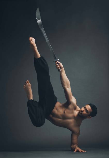 ganzkörperaufnahme eines gutaussehenden jungen mannes, der im studio einen martial-arts-kick mit einem breitschwert ausführt - shaolin stock-fotos und bilder