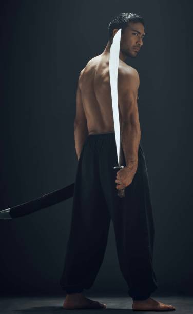 スタジオで一人で立って、ブロードソードでポーズをとるハンサムな若者の完全な長さのショット - samurai katana chinese ethnicity men ストッ�クフォトと画像