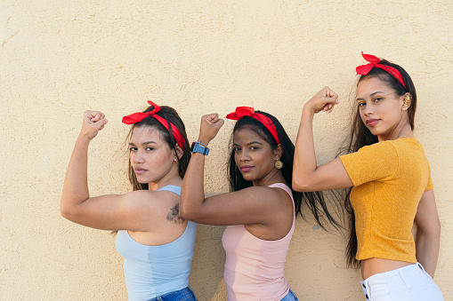 Side profile of three women wearing a headscarf and showing their strength with their arm. Concept of female power and feminism.