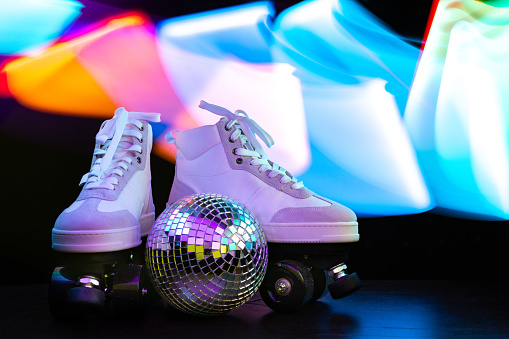 Roller skates shined with vibrant disco lights on black background.