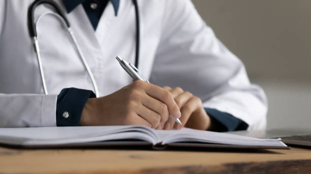 Close up cropped of female doctor therapist taking notes Close up cropped of female doctor therapist in white uniform taking notes in journal, woman physician practitioner gp filling medical documents, patient form, illness history, prescription general view stock pictures, royalty-free photos & images