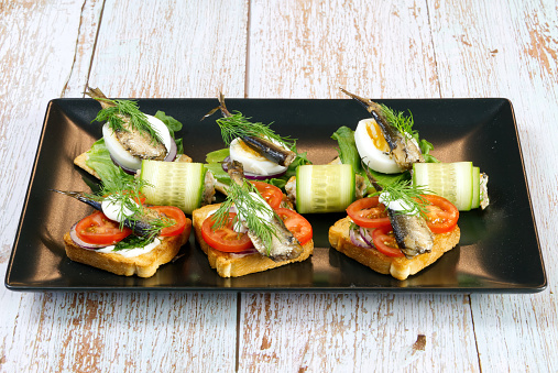 a delicious snack on a black plate. Toast with sprats, egg, tomatoes and onions. close up