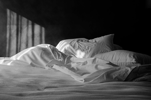An unmade bed with white linens with morning sunlight.