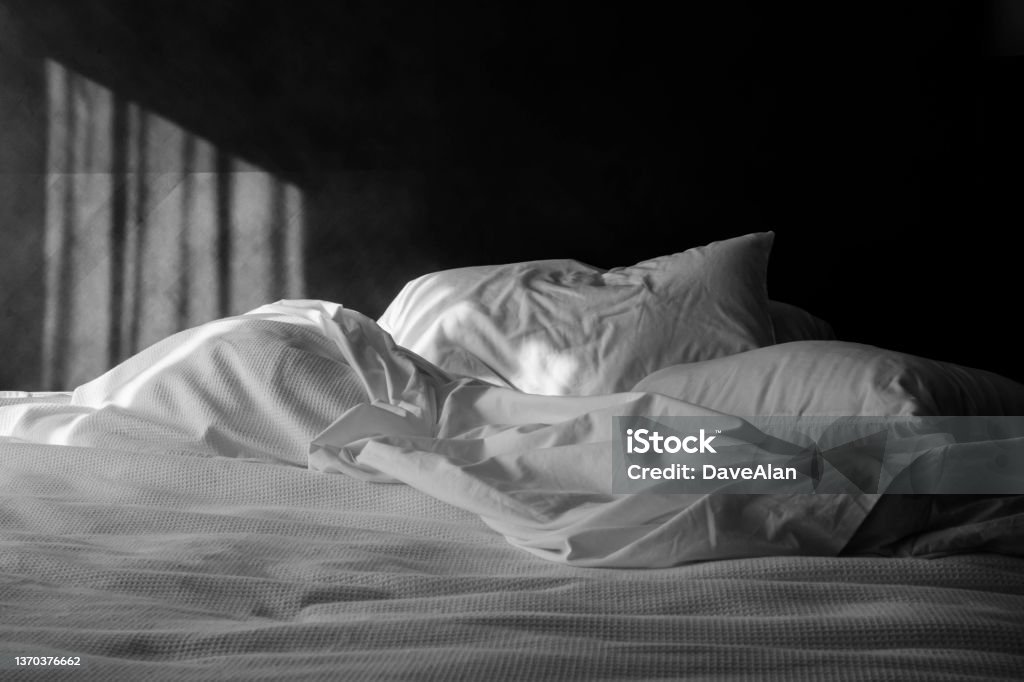 Unmade Messy Bed Pillows. An unmade bed with white linens with morning sunlight. Sheet - Bedding Stock Photo