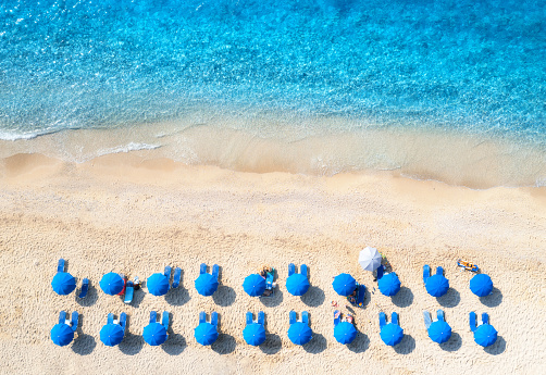 Aerial view of blue sea, sandy beach with sun beds and umbrellas at sunset in summer. Tropical landscape with turquoise water, people, deck chair. Travel and vacation. Lefkada island, Greece. Top view