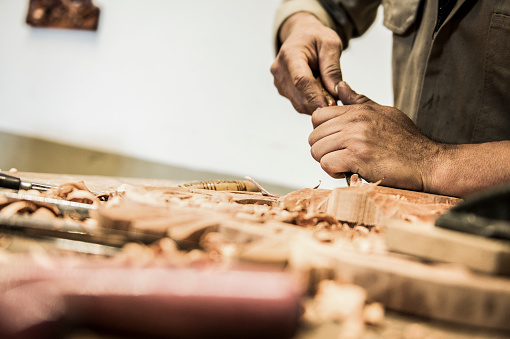 Closeup of a carpenter hands working with a chisel and carving tools on wooden workbench