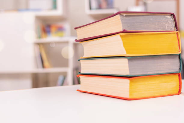 istock Thick old books with colorful covers lie in pile on white office table against backdrop of bookshelf. 1370410646