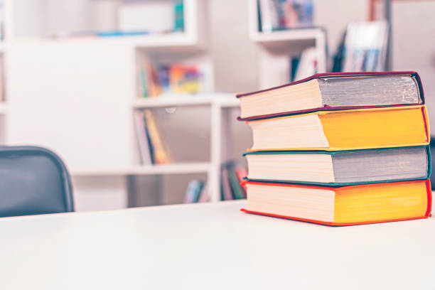 istock Thick old books with colorful covers lie in pile on white office table against backdrop of bookshelf. 1370410649