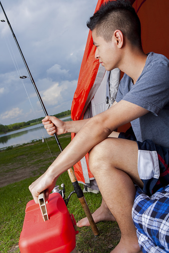 Young asian man sitting in tent holding fishing rod