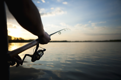Silhouette hand reeling in fishing rod